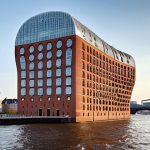 A striking wide shot of the Elbphilharmonie in Hamburg, capturing its audacious architecture. The building showcases its shimmering, wave-like glass superstructure seamlessly rising from the robust red brick base of the historic Kaispeicher A warehouse. It stands majestically anchored on the Elbe River, with reflections of the sky and water dancing on its multifaceted facade, symbolizing a fusion of past and future.